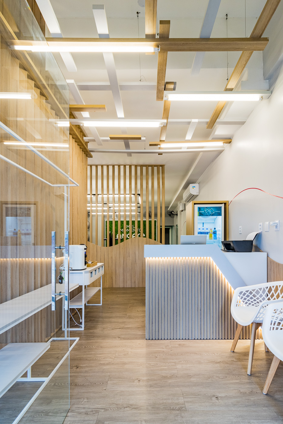 Espaço de atendimento com balcão de recepção, vitrine de produtos, ripado de madeira e iluminação linear no teto