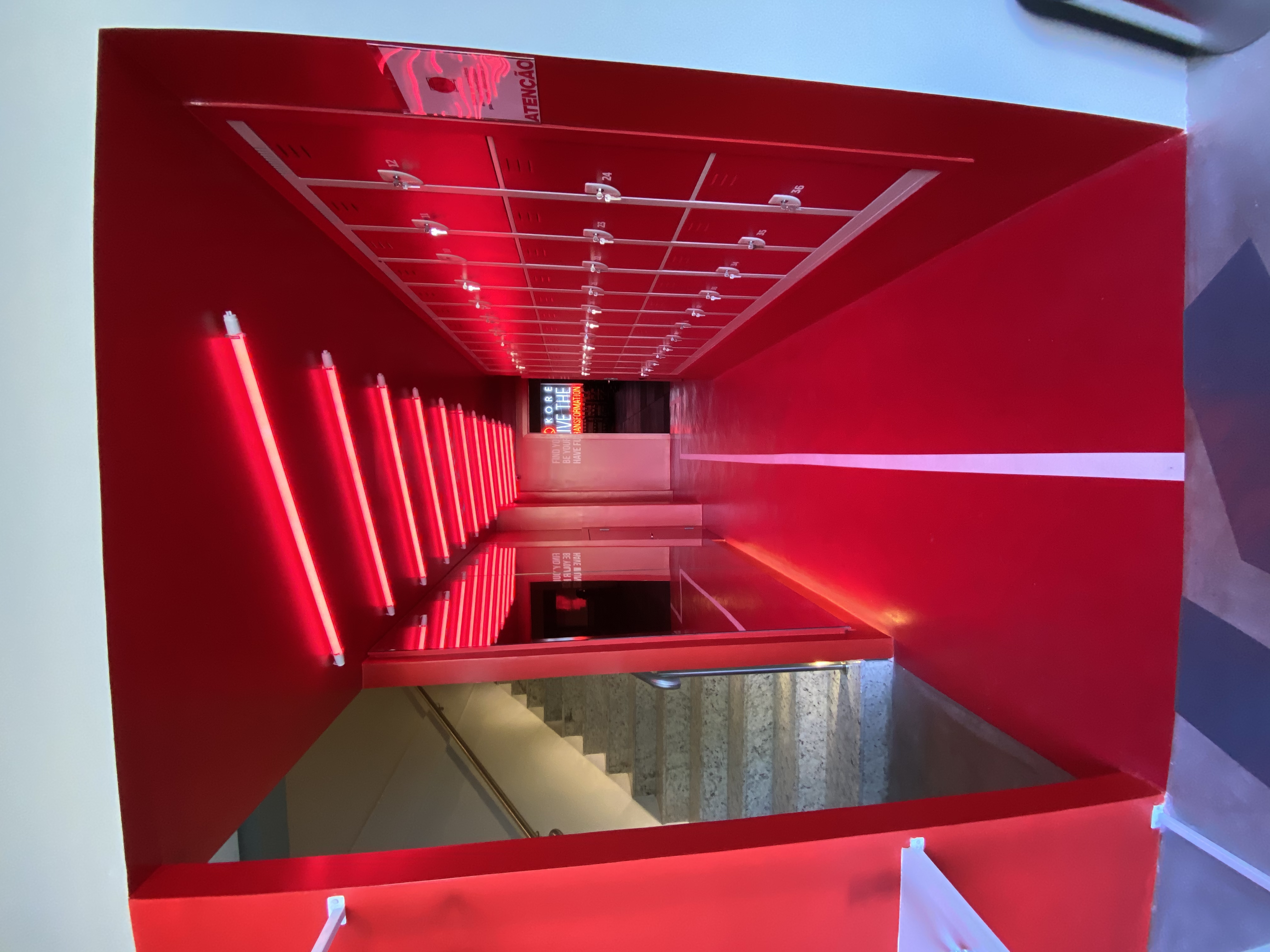 Corredor de armários da academia KORE, todo em vermelho, com tubos de luz no teto