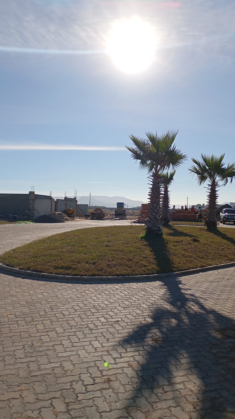 Loteamento em implantação: via pavimentada, canteiro central com paisagismo e obras ao fundo