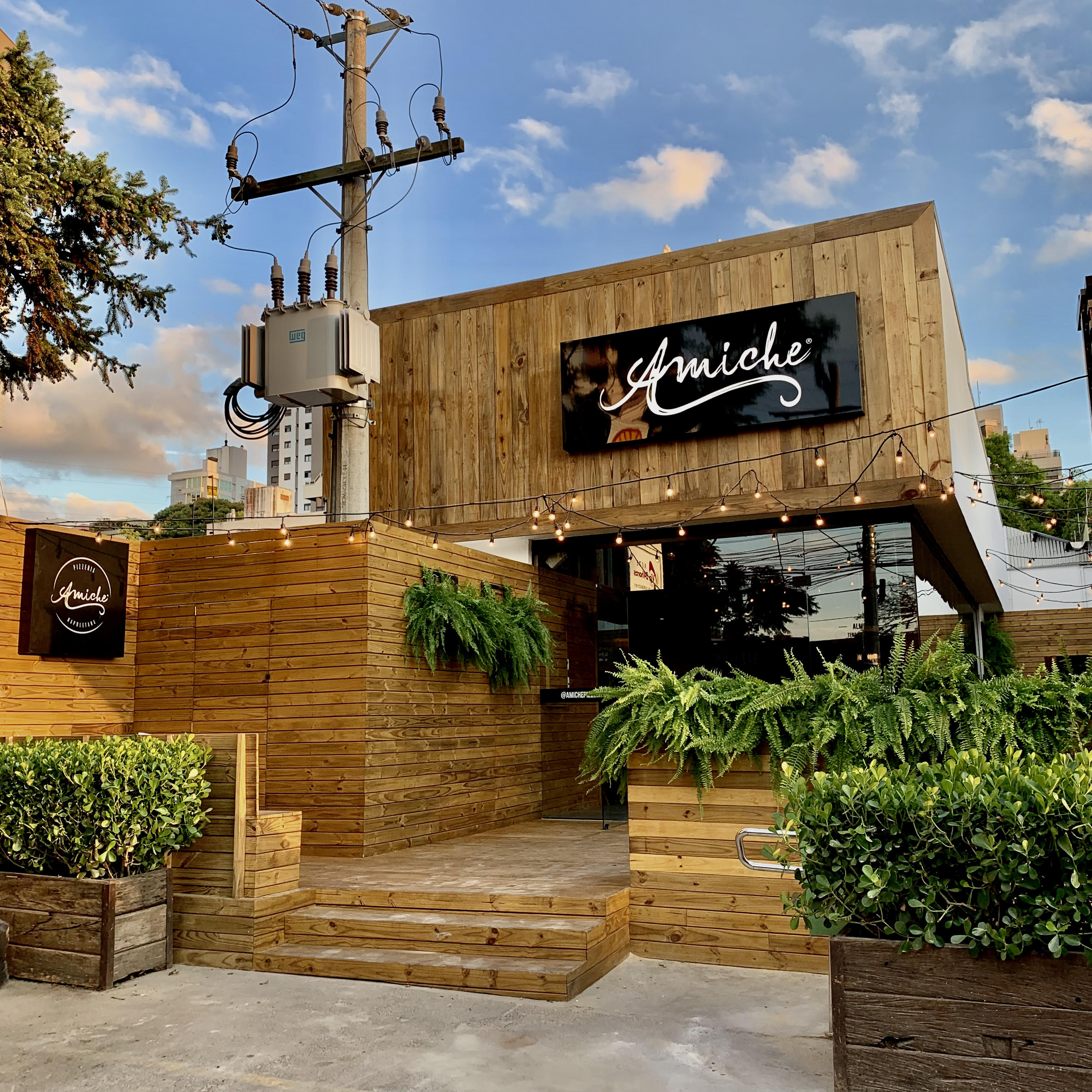 Restaurante Amiche: fachada em madeira com letreiro iluminado e deck de acesso